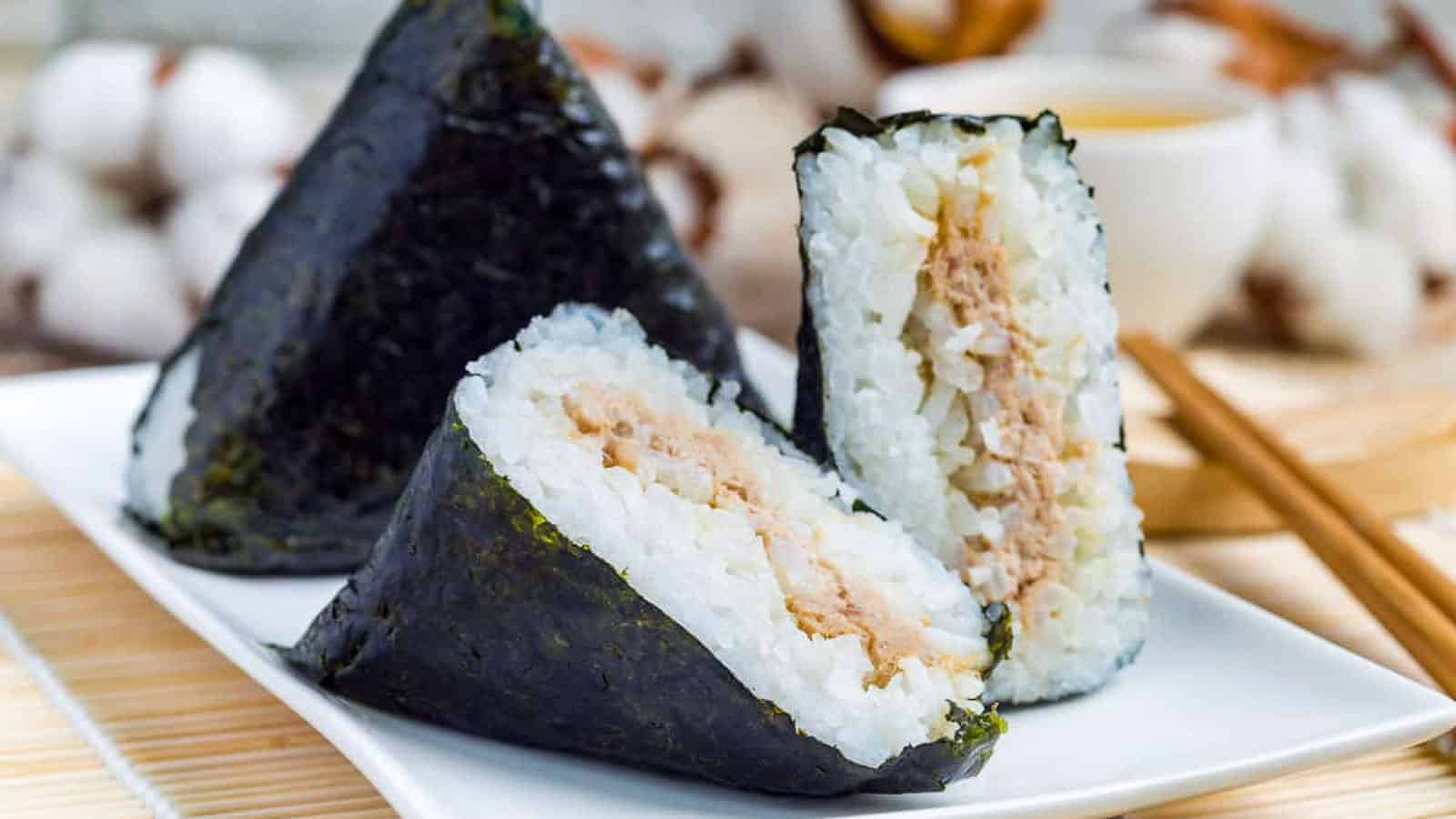 Two pieces of onigiri on a plate with chopsticks.