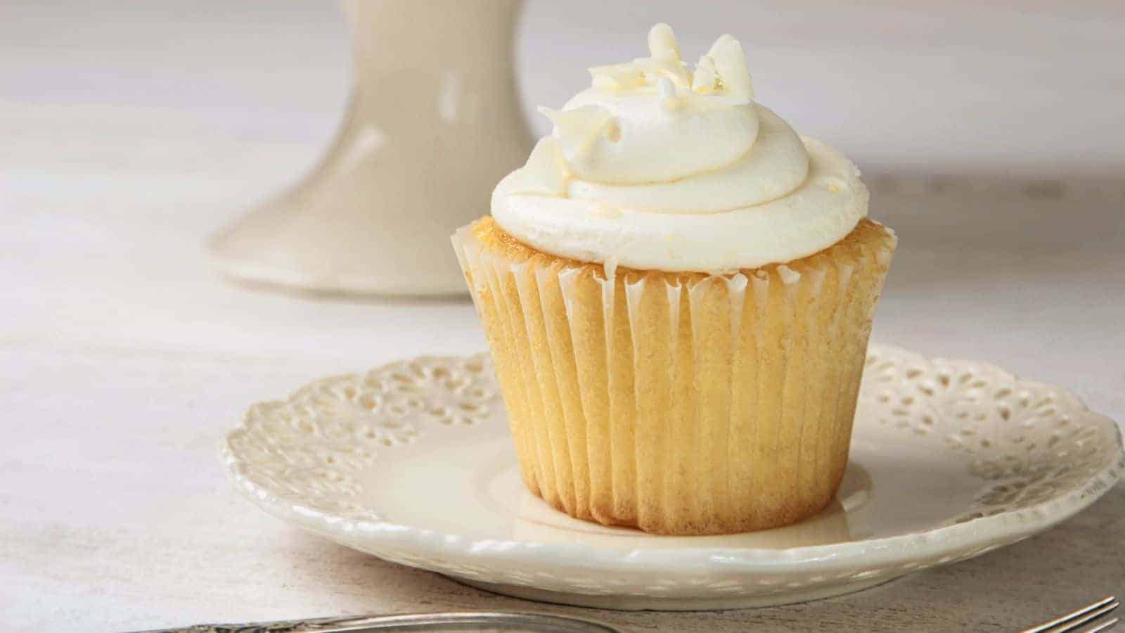 Vanilla cupcake with frosting on white china plate.