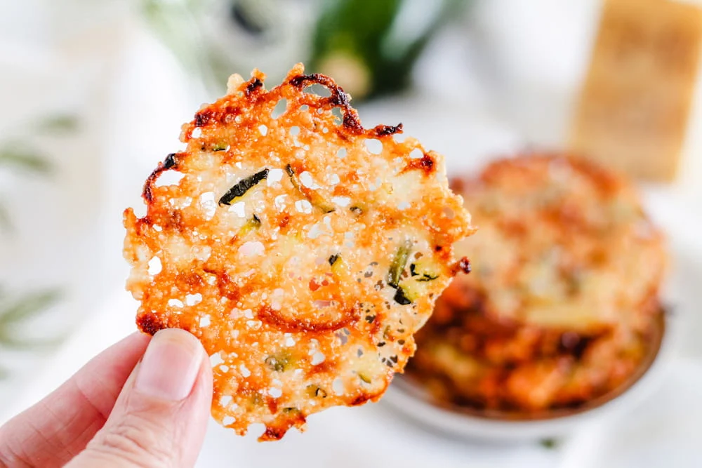 A hand holding a zucchini parmesan chip.