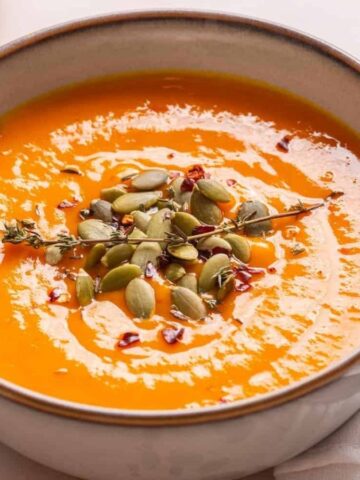 An image of acorn squash soup in a bowl garnished with thyme.