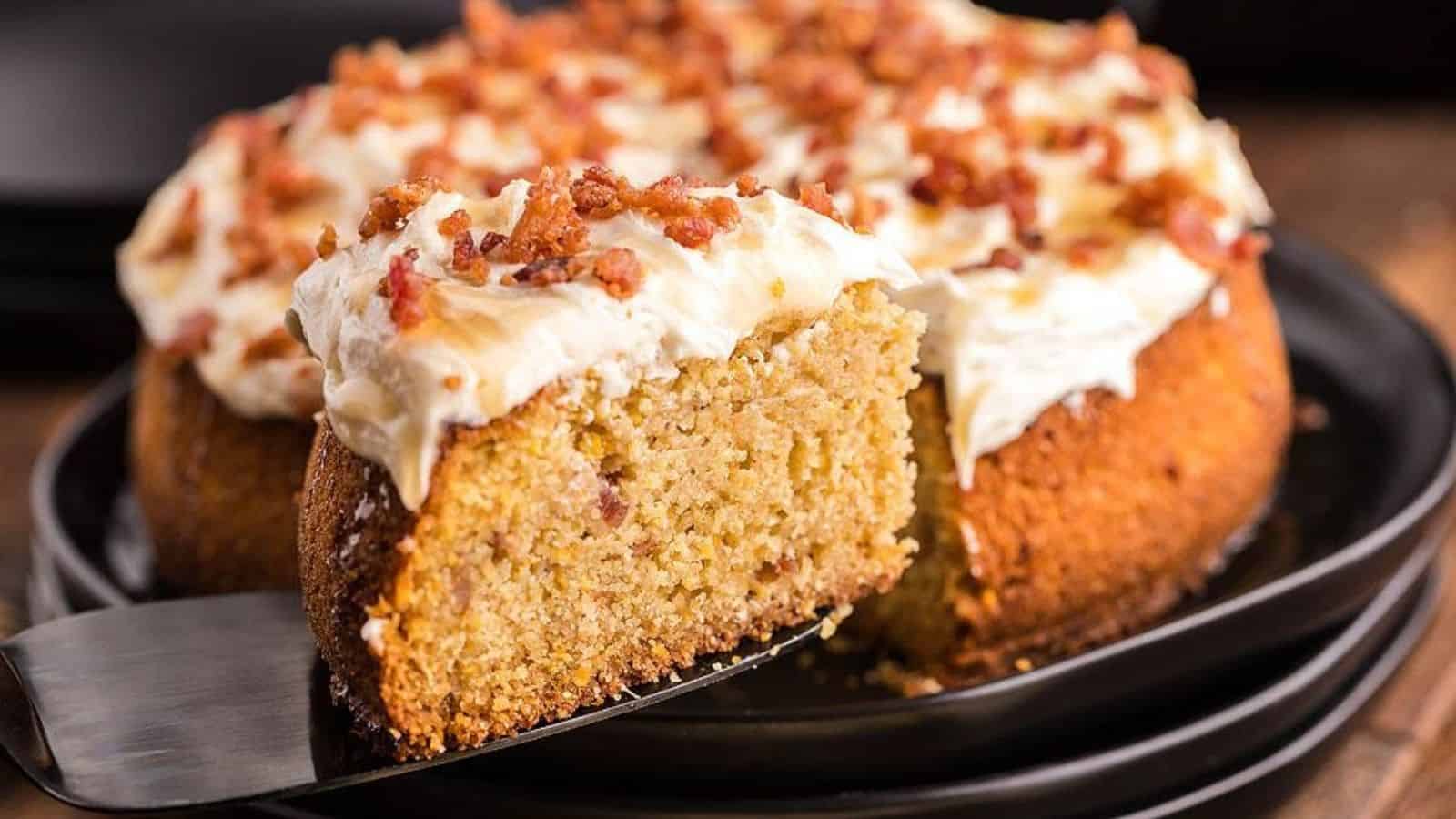 A slice of air fryer  vornbread cake with candied bacon and honey buttercream being taken.