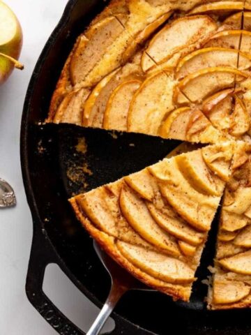 An apple cake baked in a cast iron skillet, cut into slices.