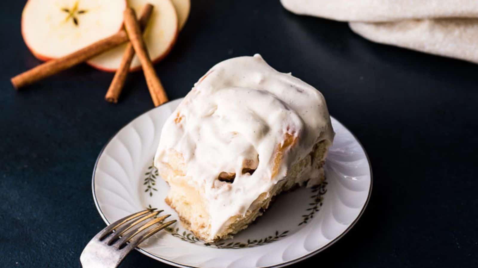 A pan of freshly baked and frosted apple cinnamon rolls on a dark blue background.