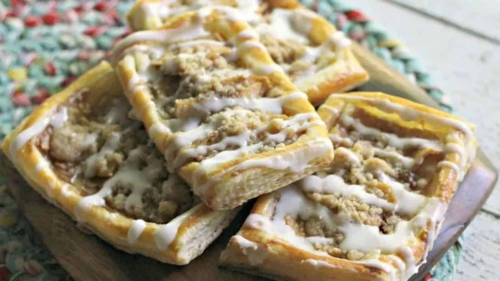 Four squares of pastry with icing on a wooden cutting board.