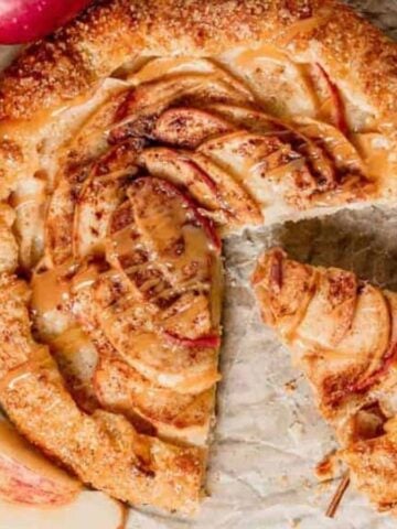 Overhead shot of an apple galette on parchment with fresh apples on the side.