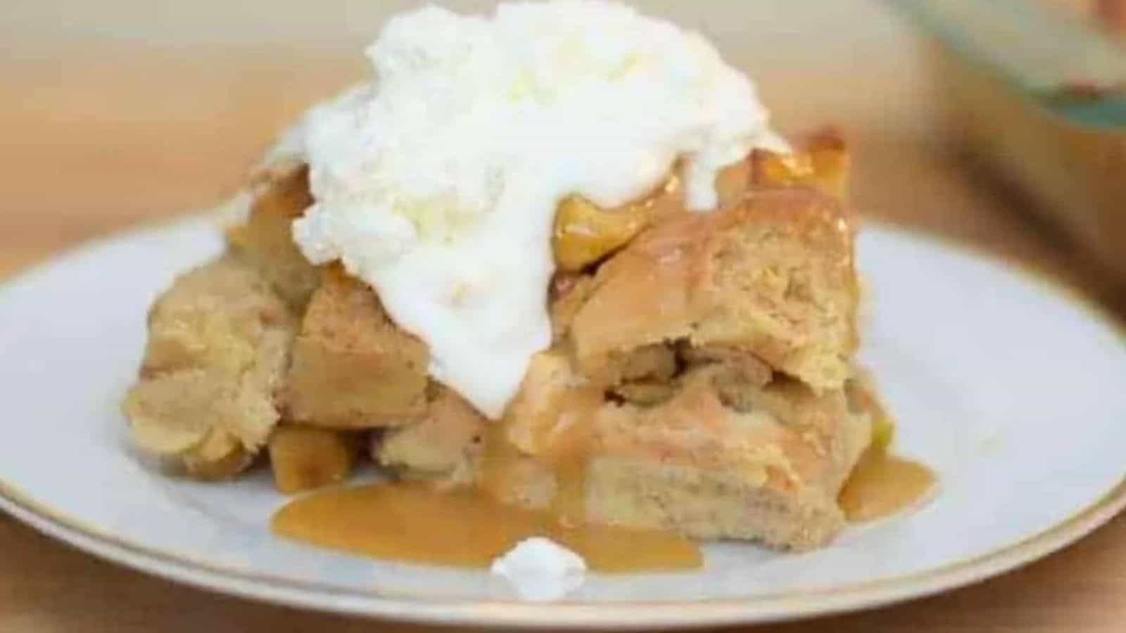 Image shows a head on close up shot of a slice of Apple Pie Bread Pudding topped with whipped cream.