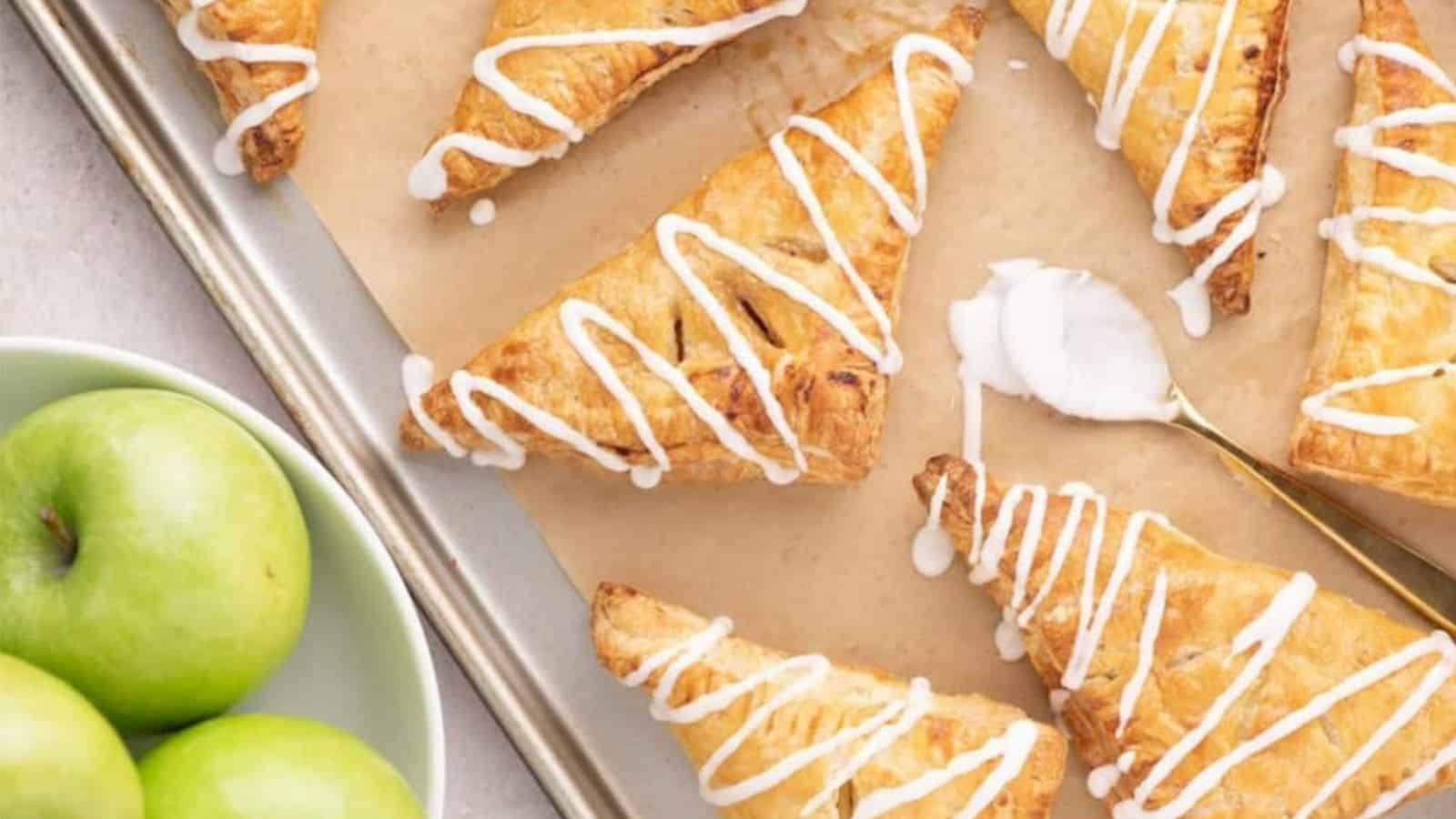 Overhead image of apple turnovers on a baking tray with green apples in a separate bowl.