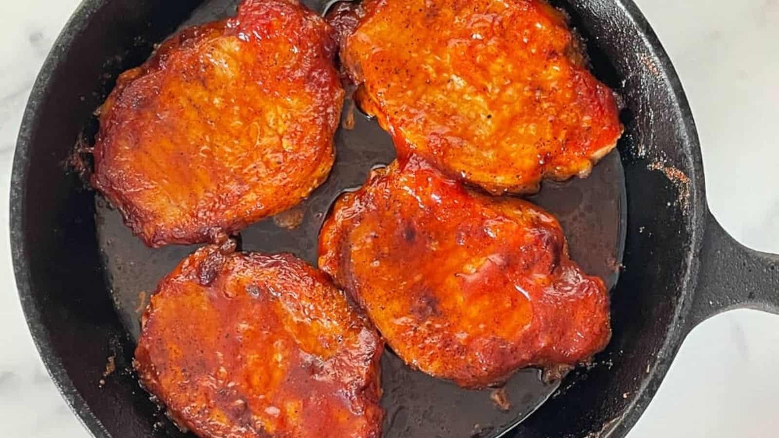 Pork chops in a cast iron skillet with bbq sauce on the chops.