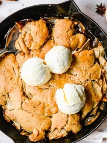 An overhead image of bisquick apple cobbler in a skillet pan topped with vanilla ice cream.