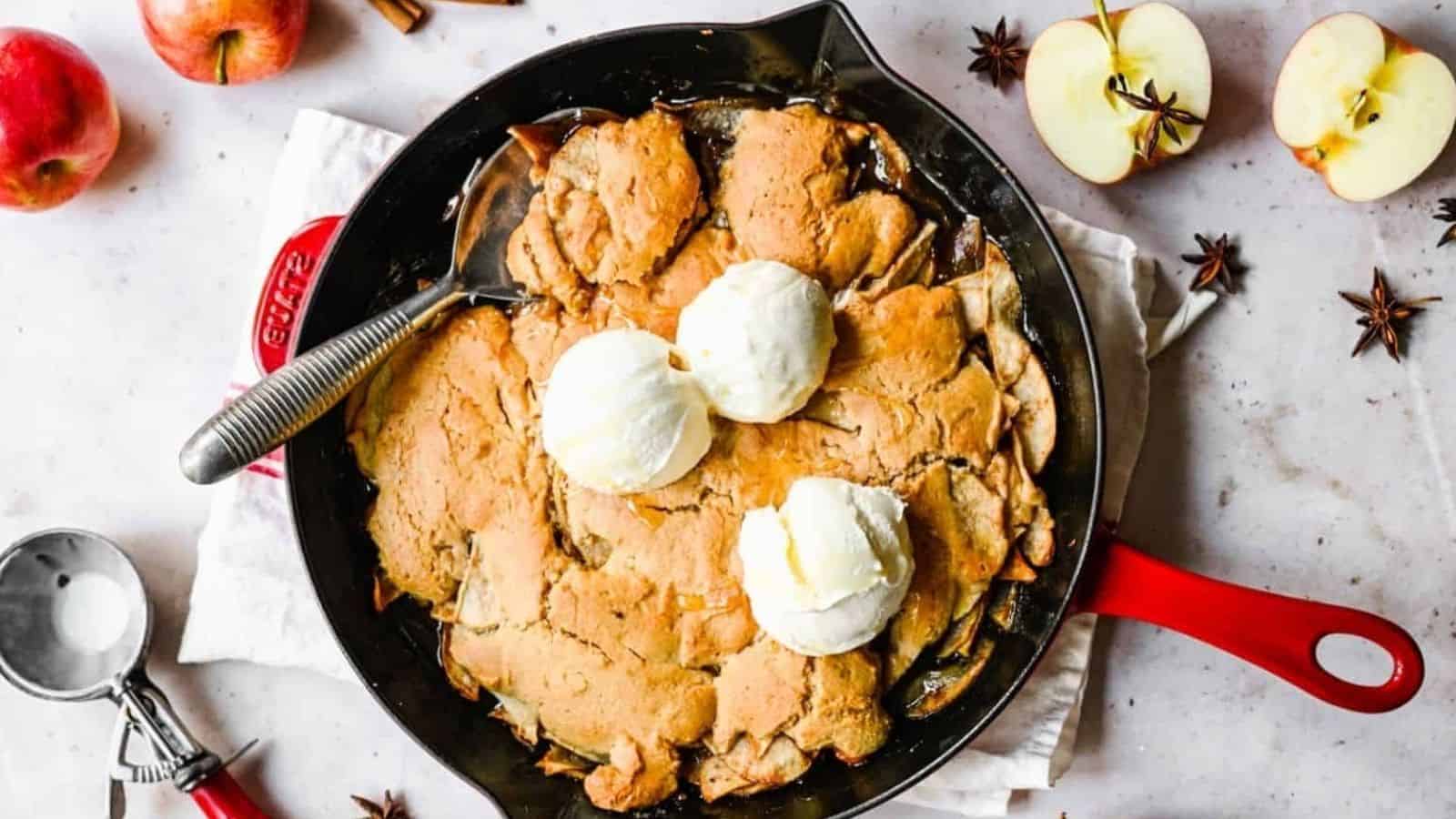 An overhead image of bisquick apple cobbler in a skillet pan topped with vanilla ice cream.