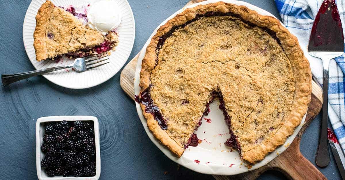 Overhead shot of blackberry crumble pie with one slice on a serving plate.