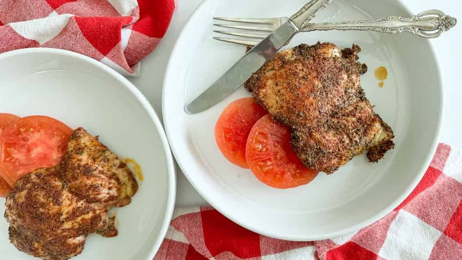 Chicken coated in seasoning on a plate with tomatoes.