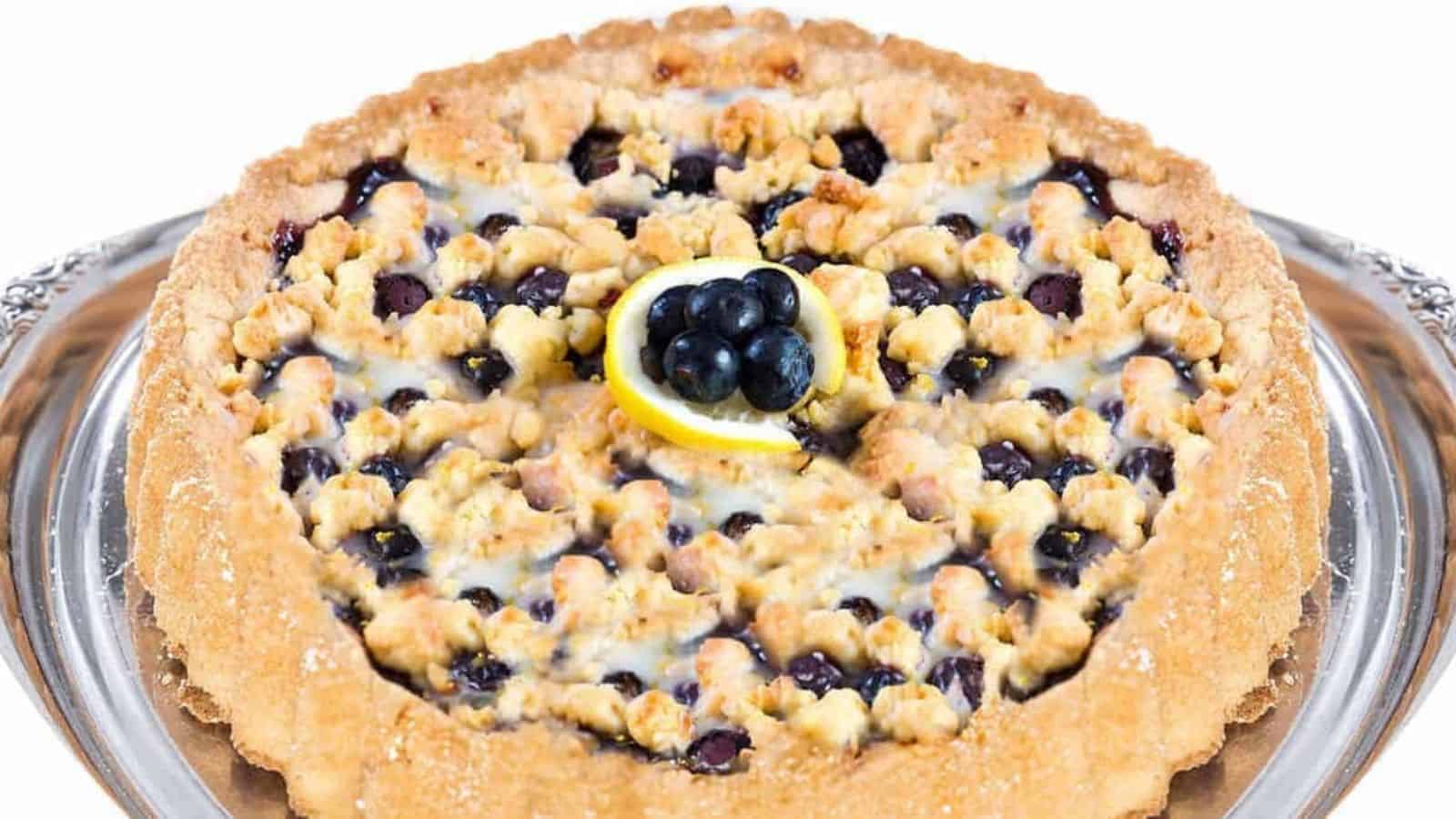 A close up image of a freshly baked blueberry tart topped with shortbread crumbs.