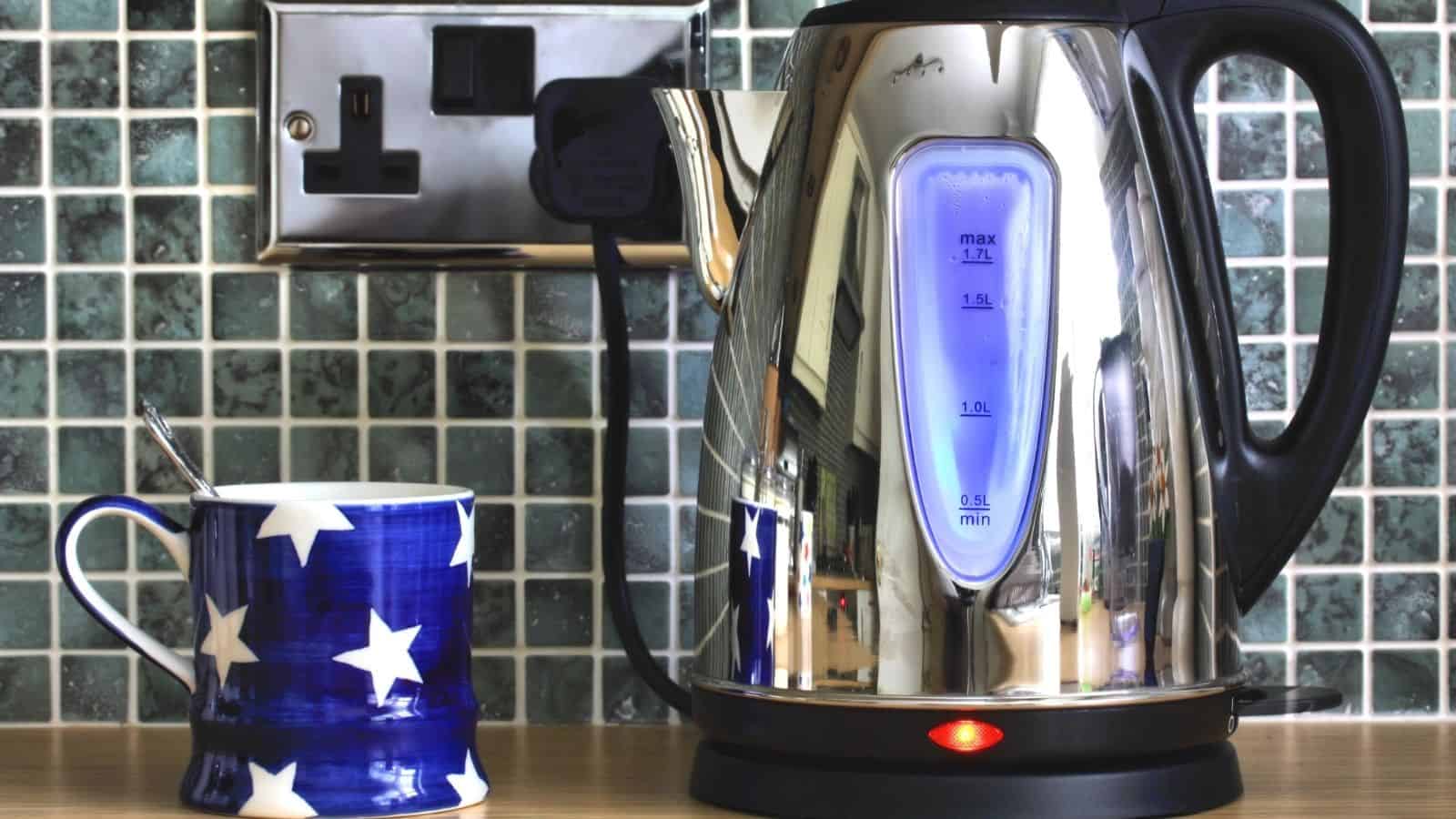 Electric kettle and cup on top of a wooden table.
