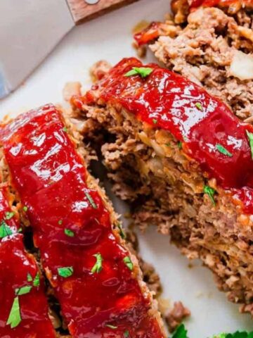 Meatloaf on a white plate cut into slices with fresh parsley garnish.