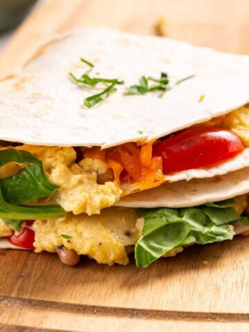An image of two breakfast quesadillas on a wooden cutting board.