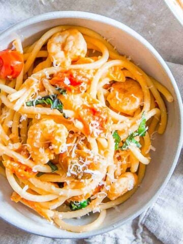 Bucatini pasta with shrimp in a white bowl.