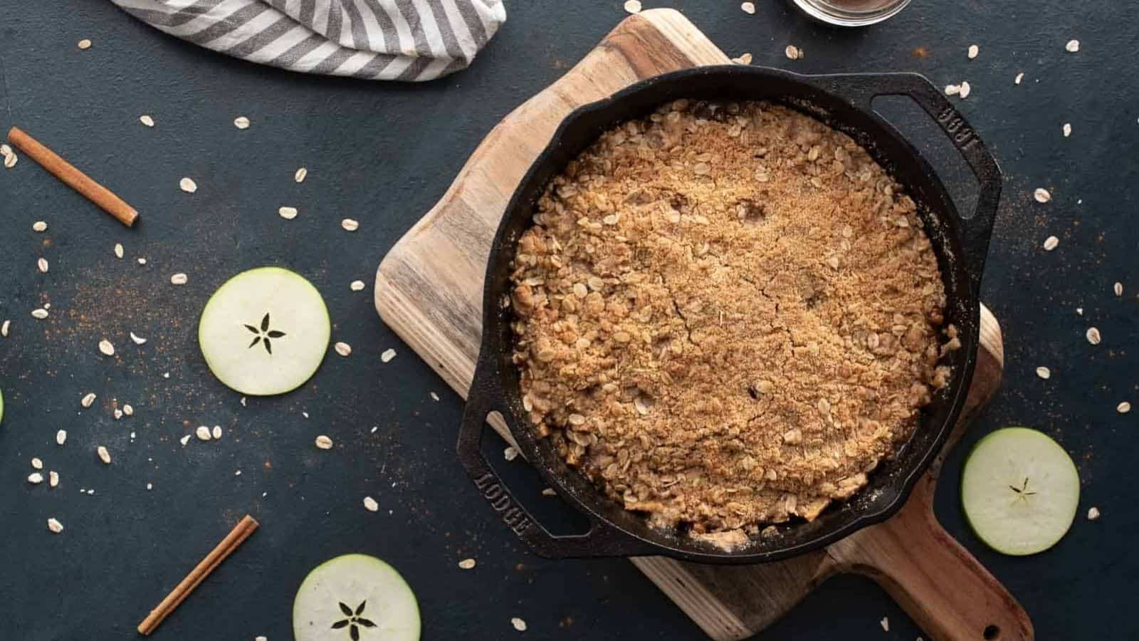 A butterscotch apple crumble in a cast iron skillet on a wooden cutting board.