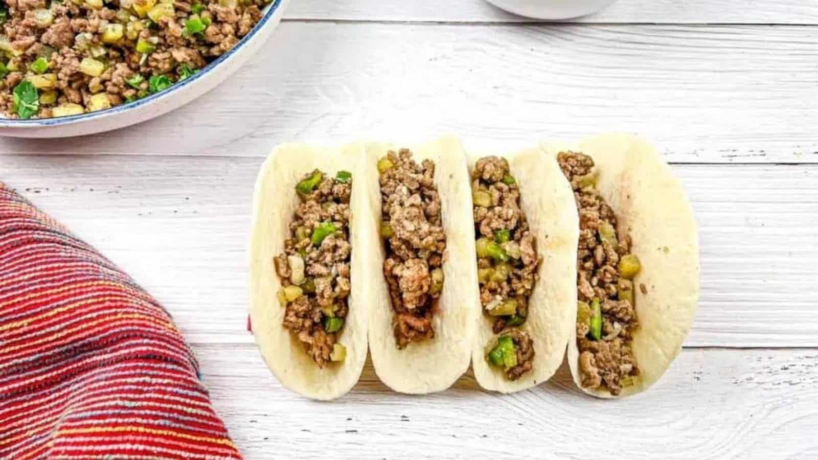 Four tacos with carne molida on a wooden surface.