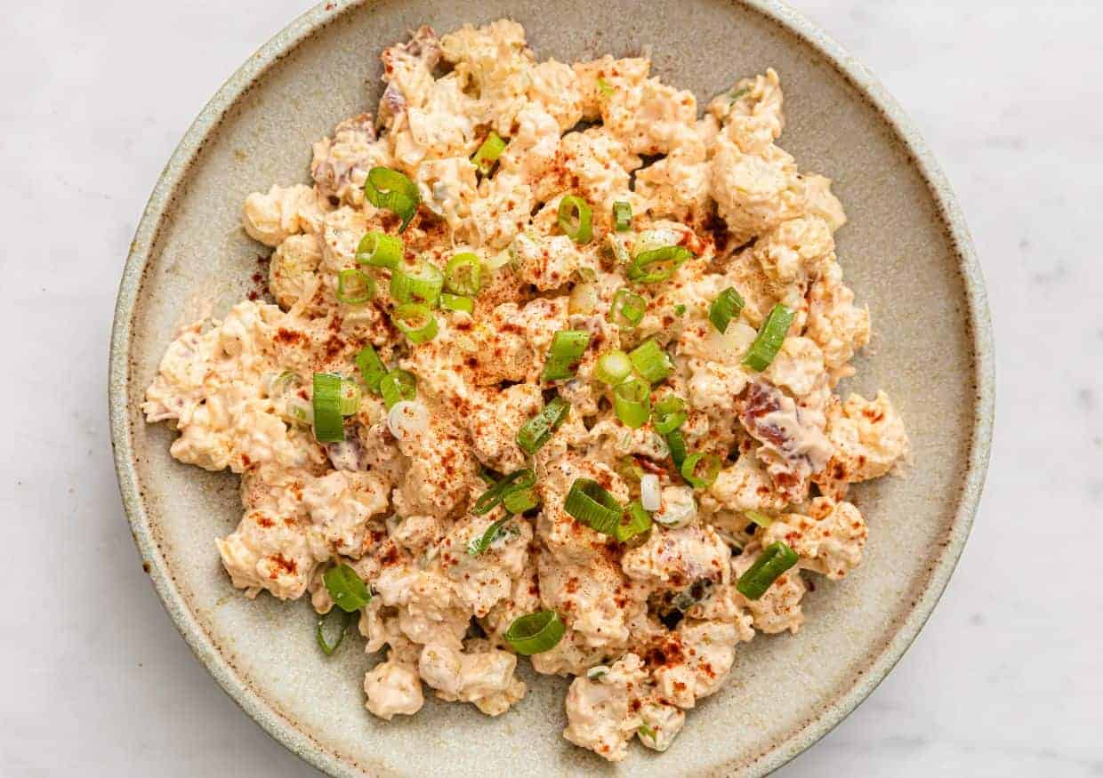 Cauliflower potato salad garnished with green onions in a bowl with a fork.