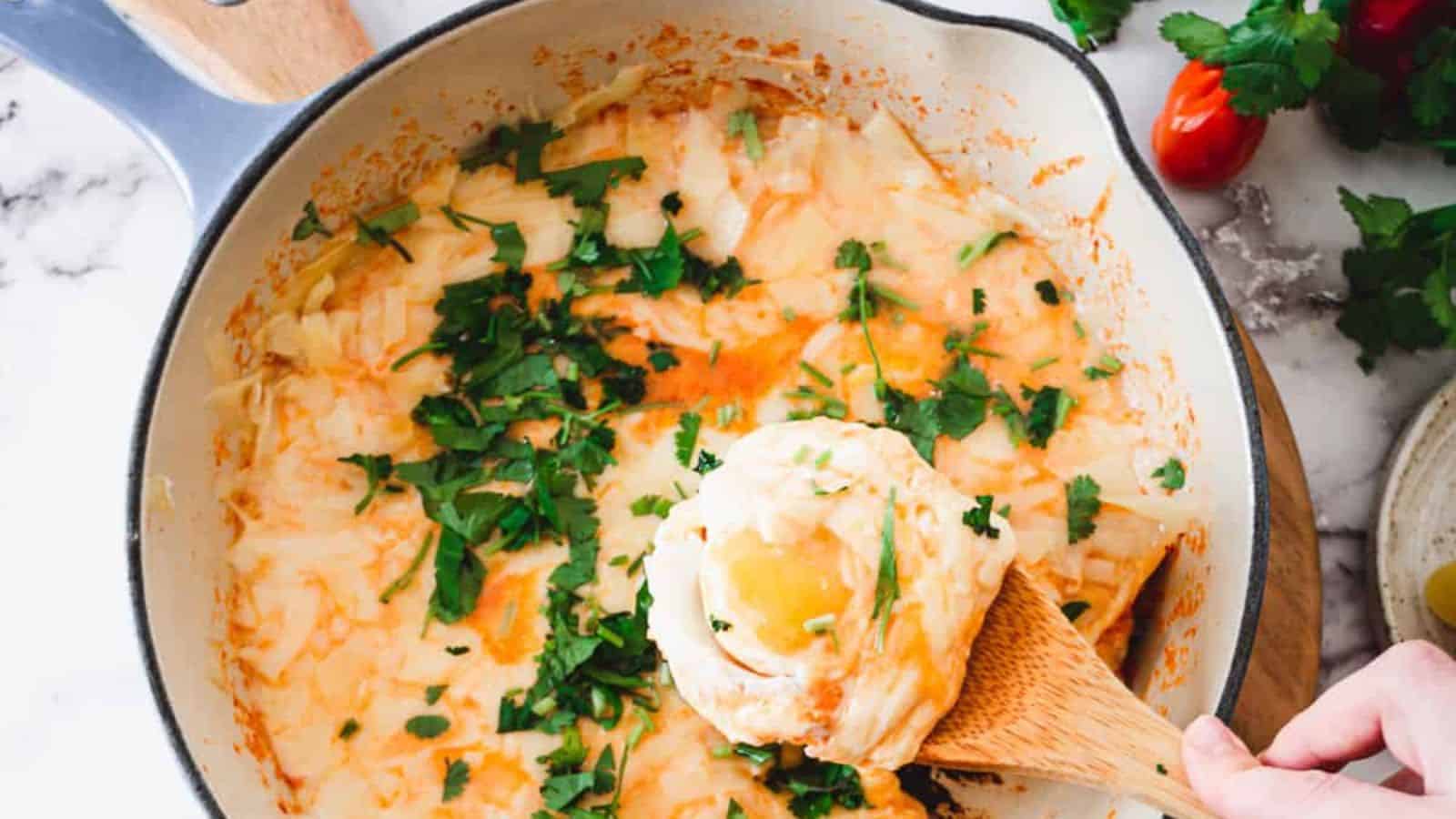 A person scooping a dish of eggs in a skillet.