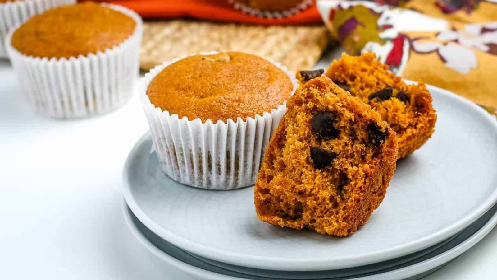 Chocolate chip pumpkin muffins on a plate with one cut open to show the insides.