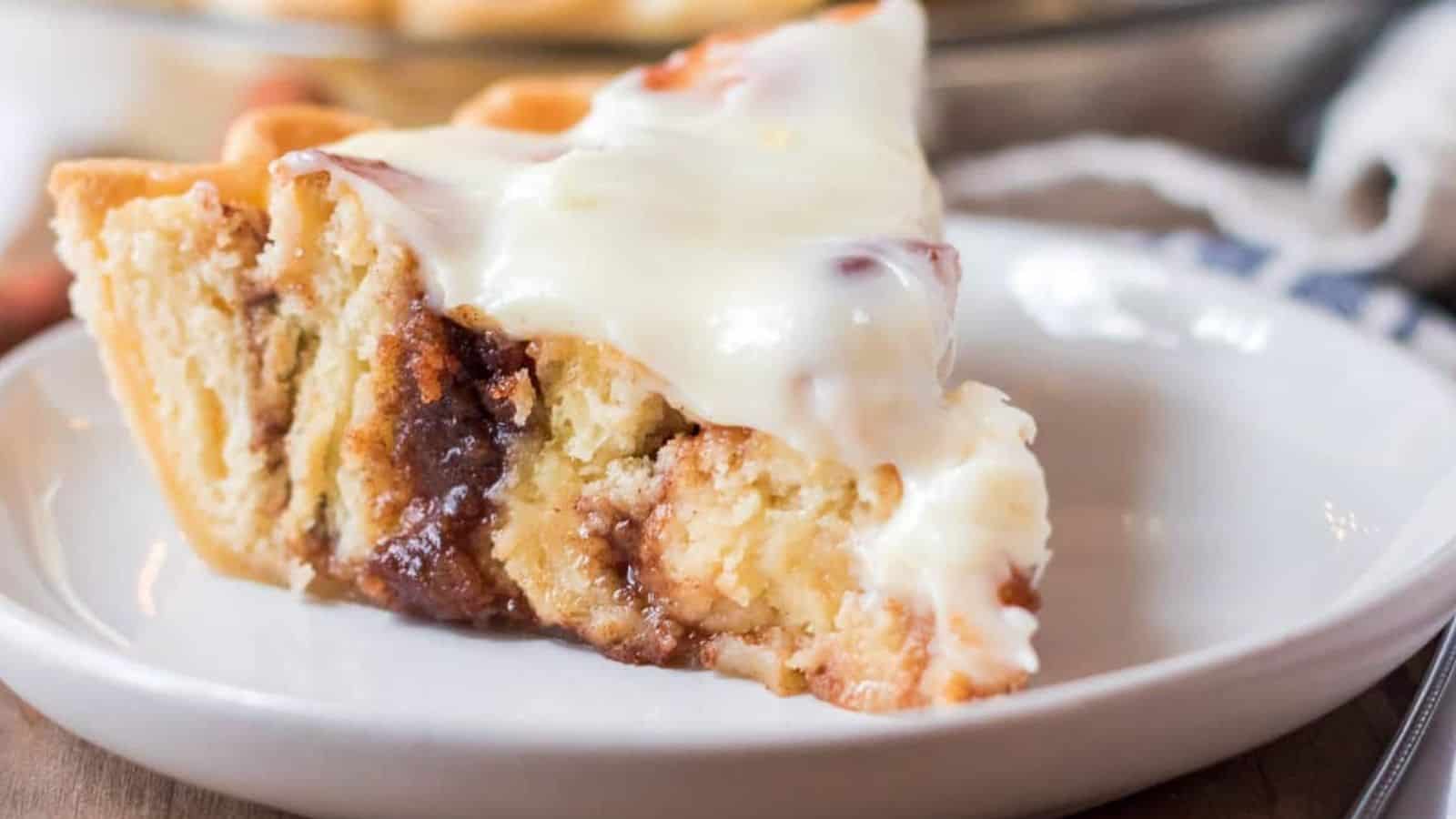 Slice of cinnamon roll pie with cream cheese icing on a white plate.