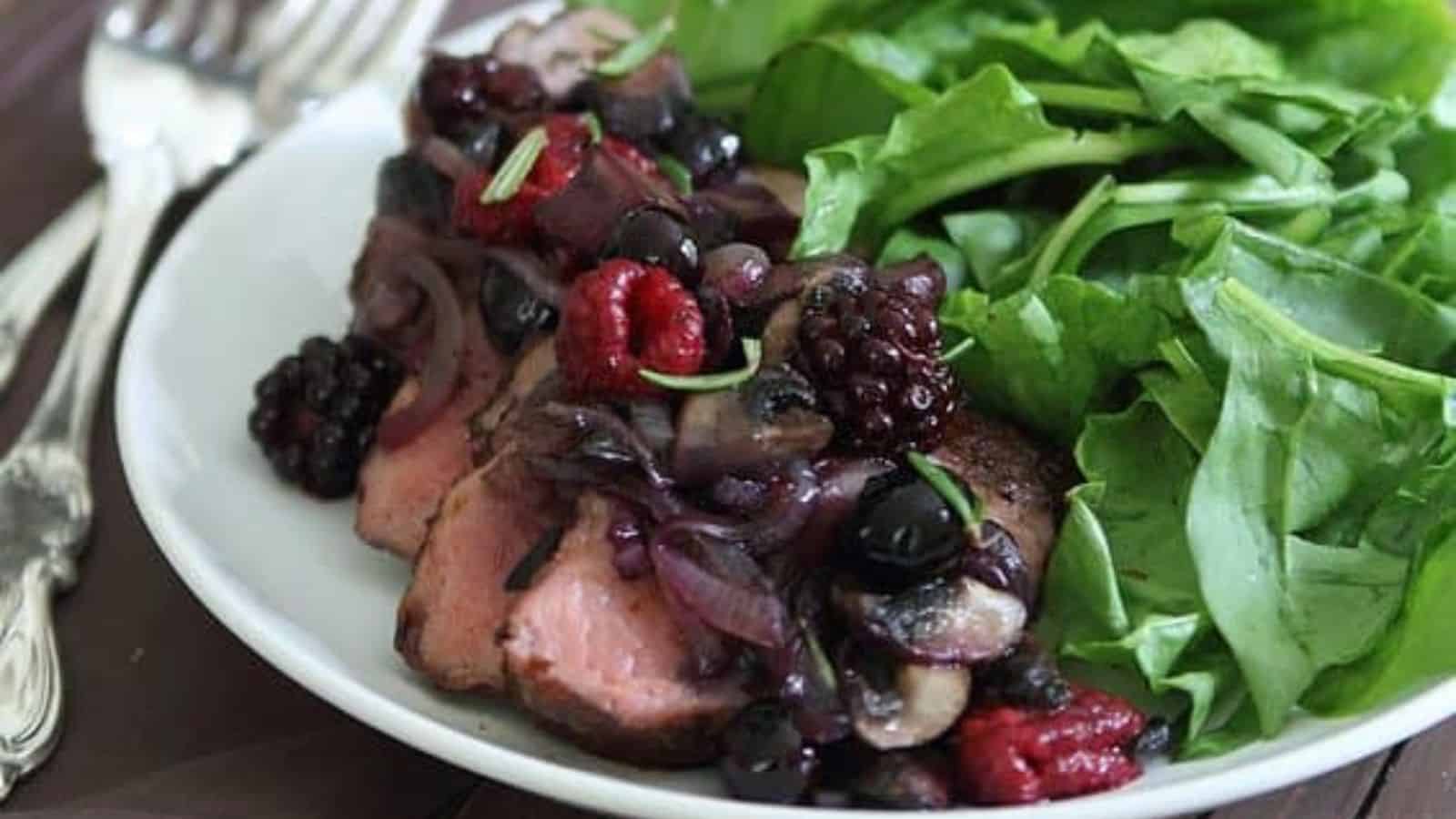 A plate of Cocoa Spiced Rubbed Pork Tenderloin with Crimini Berry Sauce and some greens.