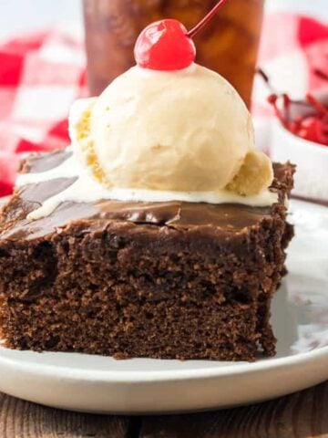 Chocolate coca cola cake on a white plate topped with ice cream and a cherry.
