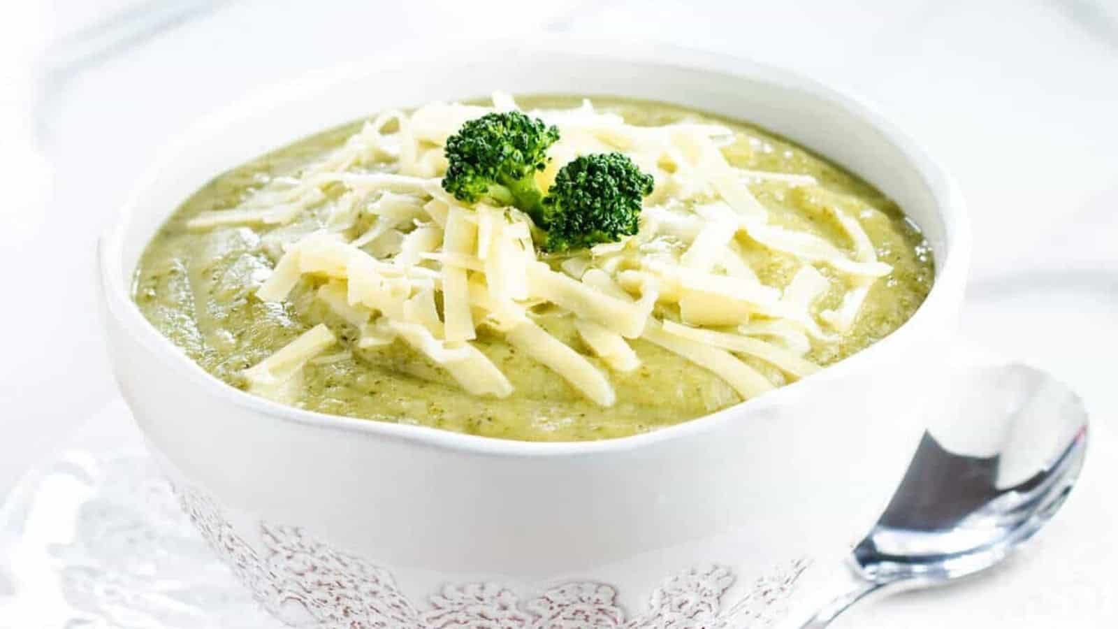 A close up image of broccoli soup in a white bowl topped with shredded cheese.