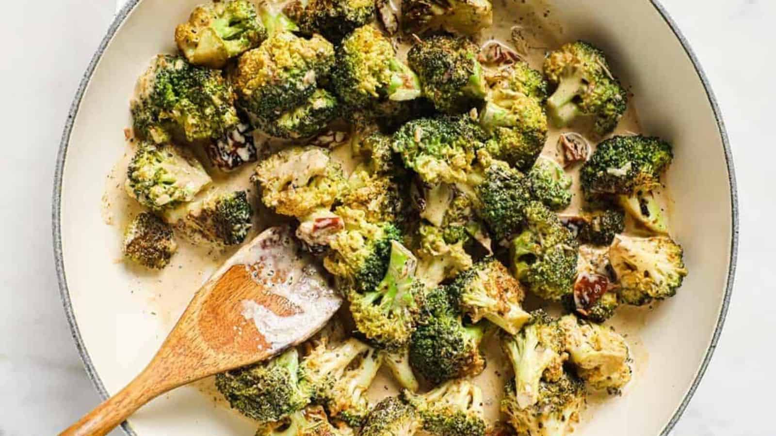 A pan of creamy broccoli with sun-dried tomatoes with a wooden spoon.