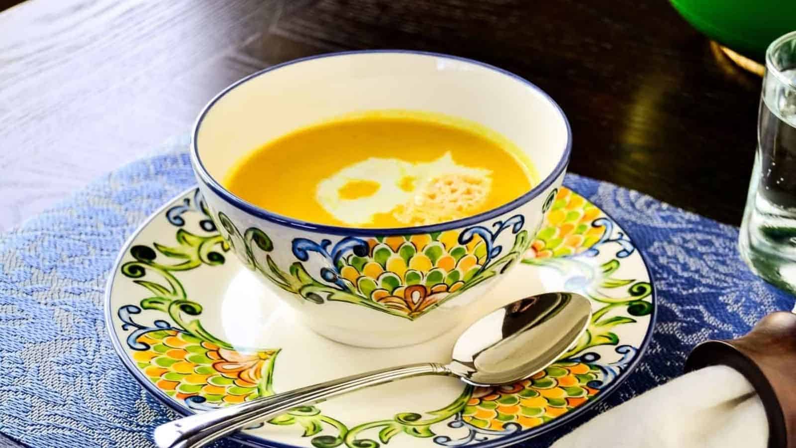 A bowl of butternut squash soup with a spoon on a colorful blue and white plate.