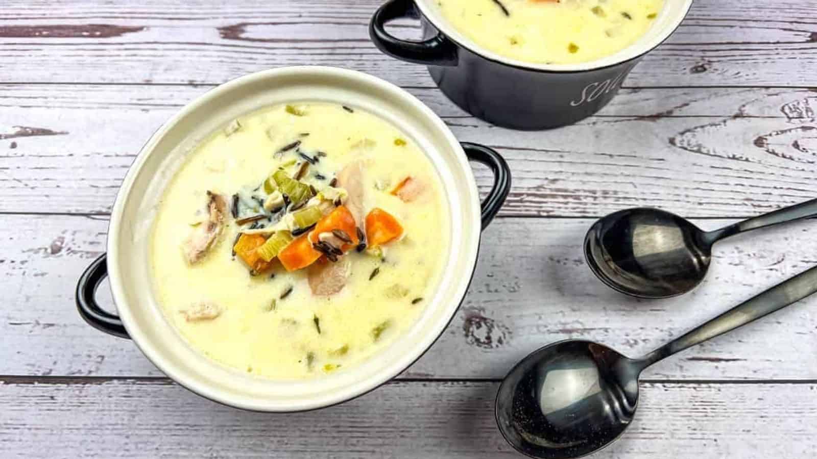 Two bowls of creamy chicken & wild rice soup on a wooden table.