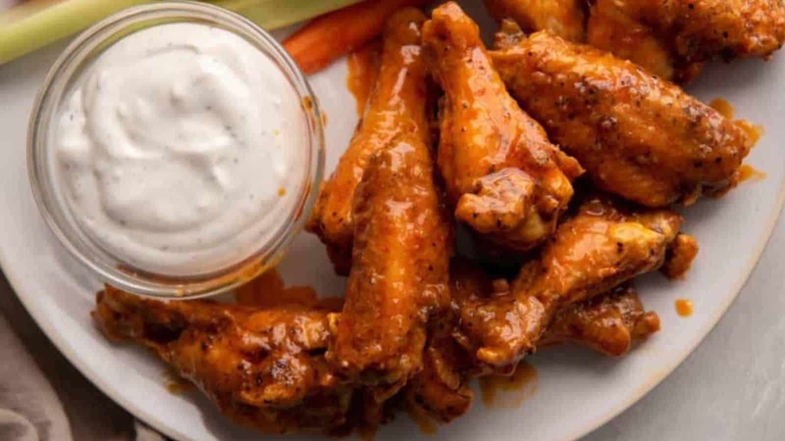 Top view of air fryer buffalo wings with a small bowl of white dip on a plate.