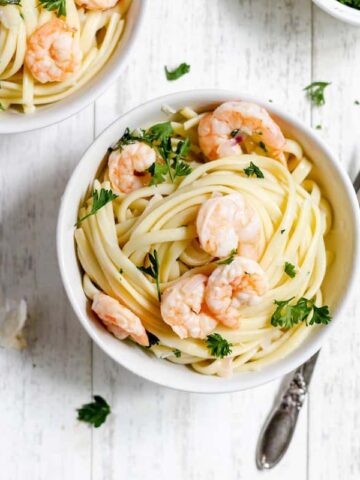 Two bowls of dairy-free shrimp scampi pasta with parsley on a wooden table.