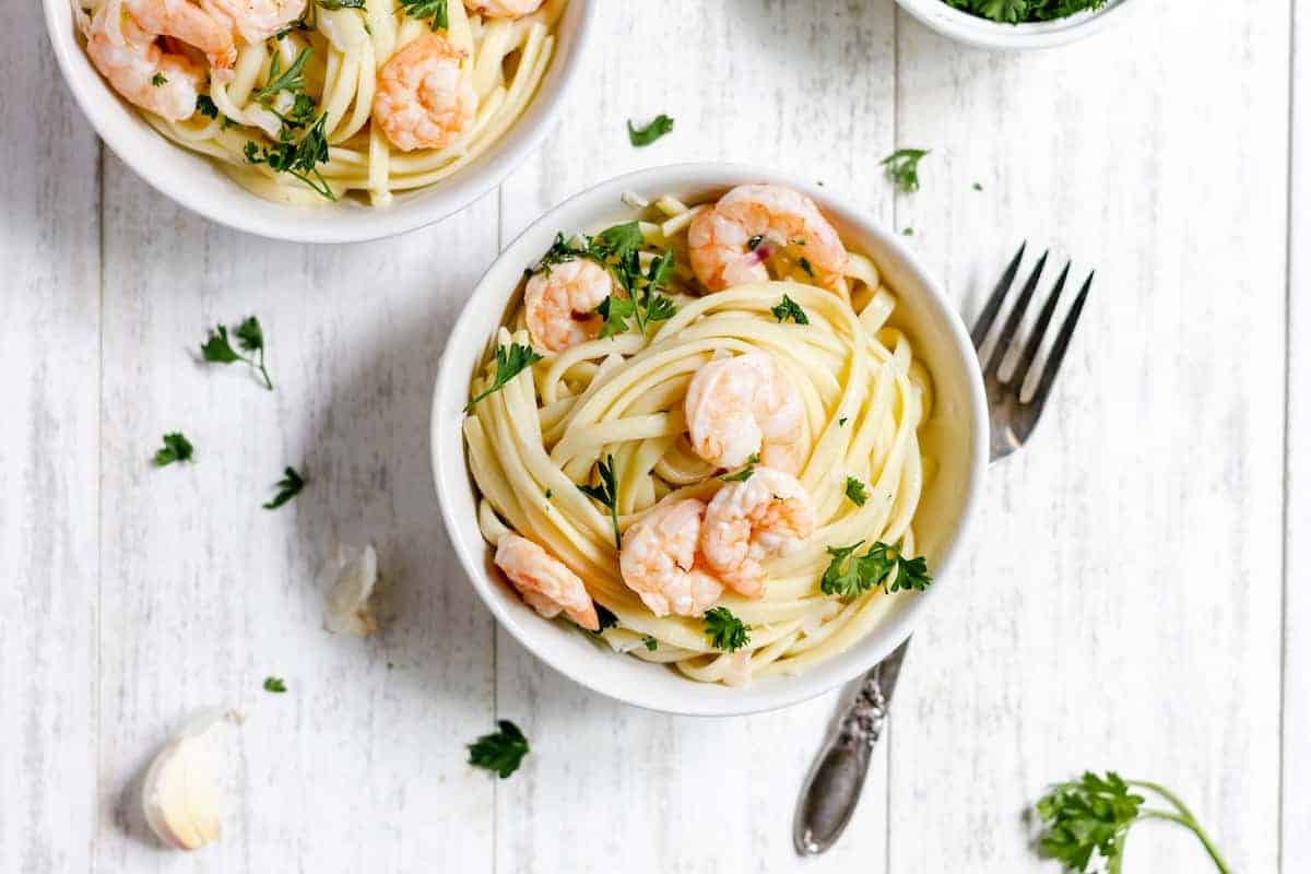 Two bowls of dairy-free shrimp scampi pasta with parsley on a wooden table.