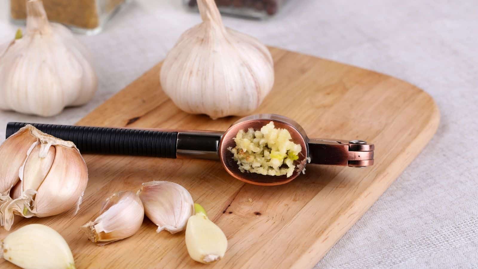 Garlic cloves and garlic press on a wooden board.