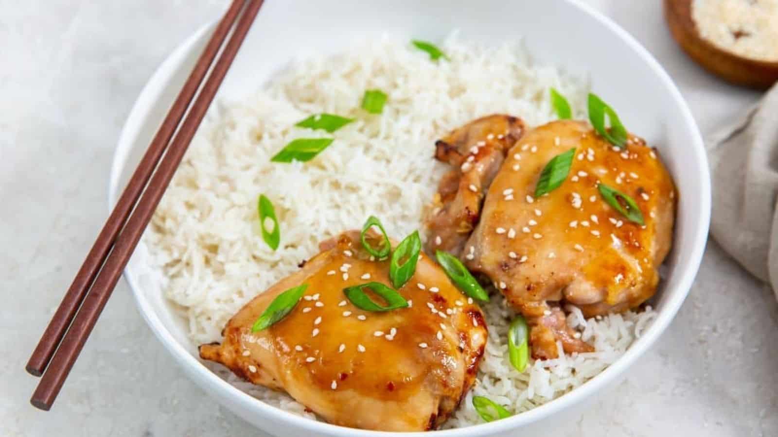 Easy Air Fryer Teriyaki Chicken Thighs in a white bowl with white rice, green onions, and sesame seeds.