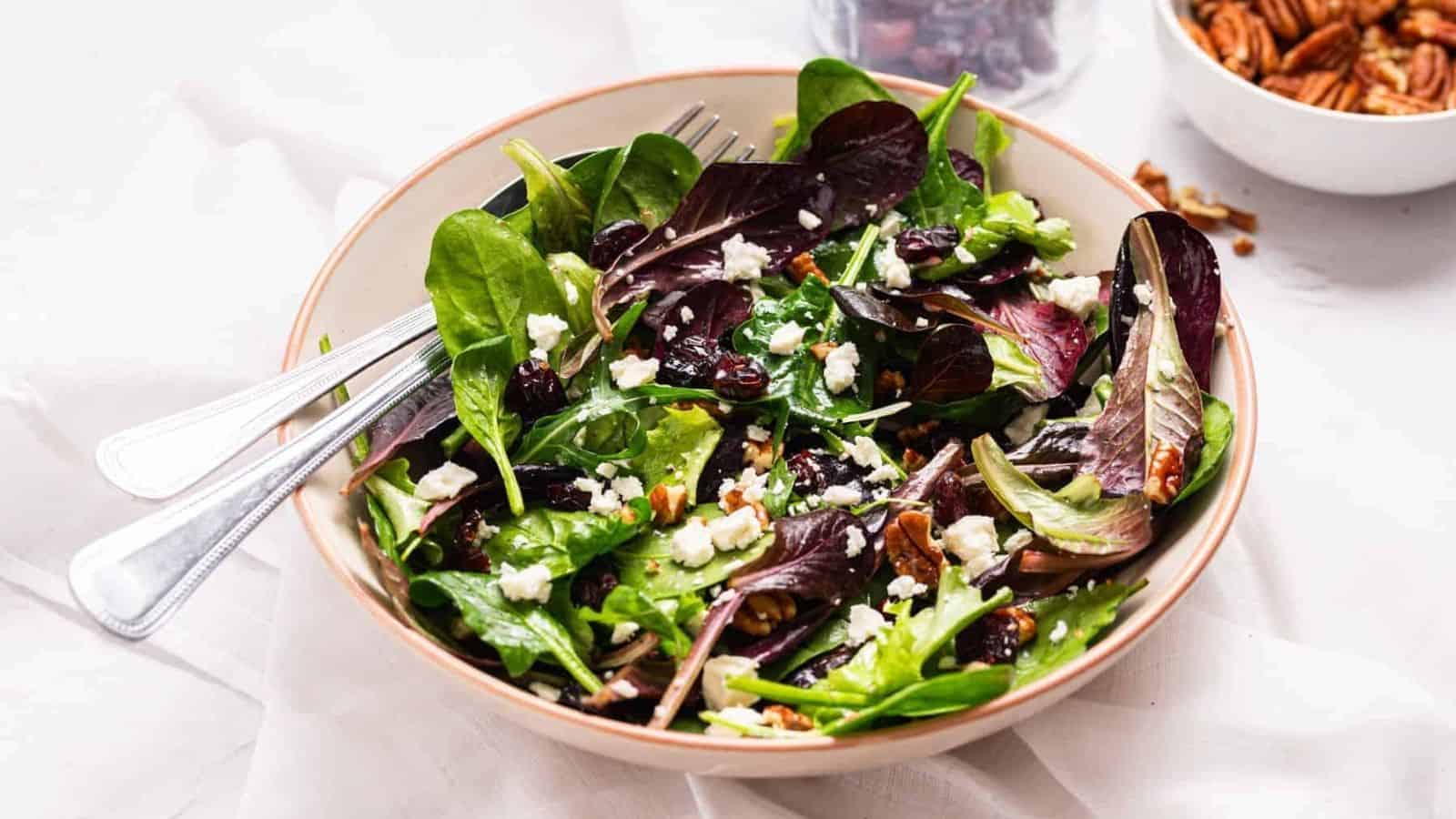 An image of cranberry salad with pecans served in a white salad bowl with a fork on the side.