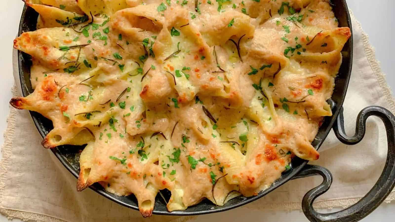 A cast iron pan filled with stuffed shells covered in cheese and a white sauce.