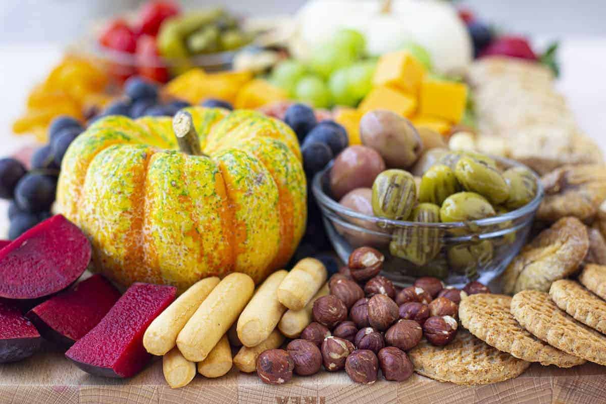 A wooden cutting board with a variety of fruits and vegetables topped with Peach Jalapeno Jam.