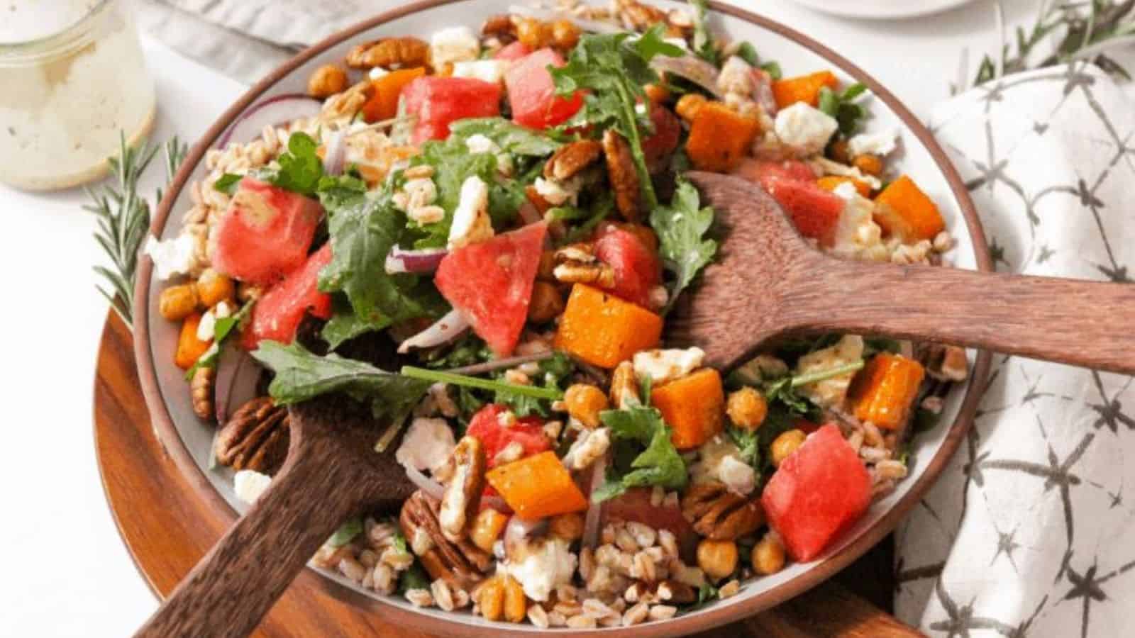 Fall harvest salad with watermelon and 2 wooden laddles on a plate.