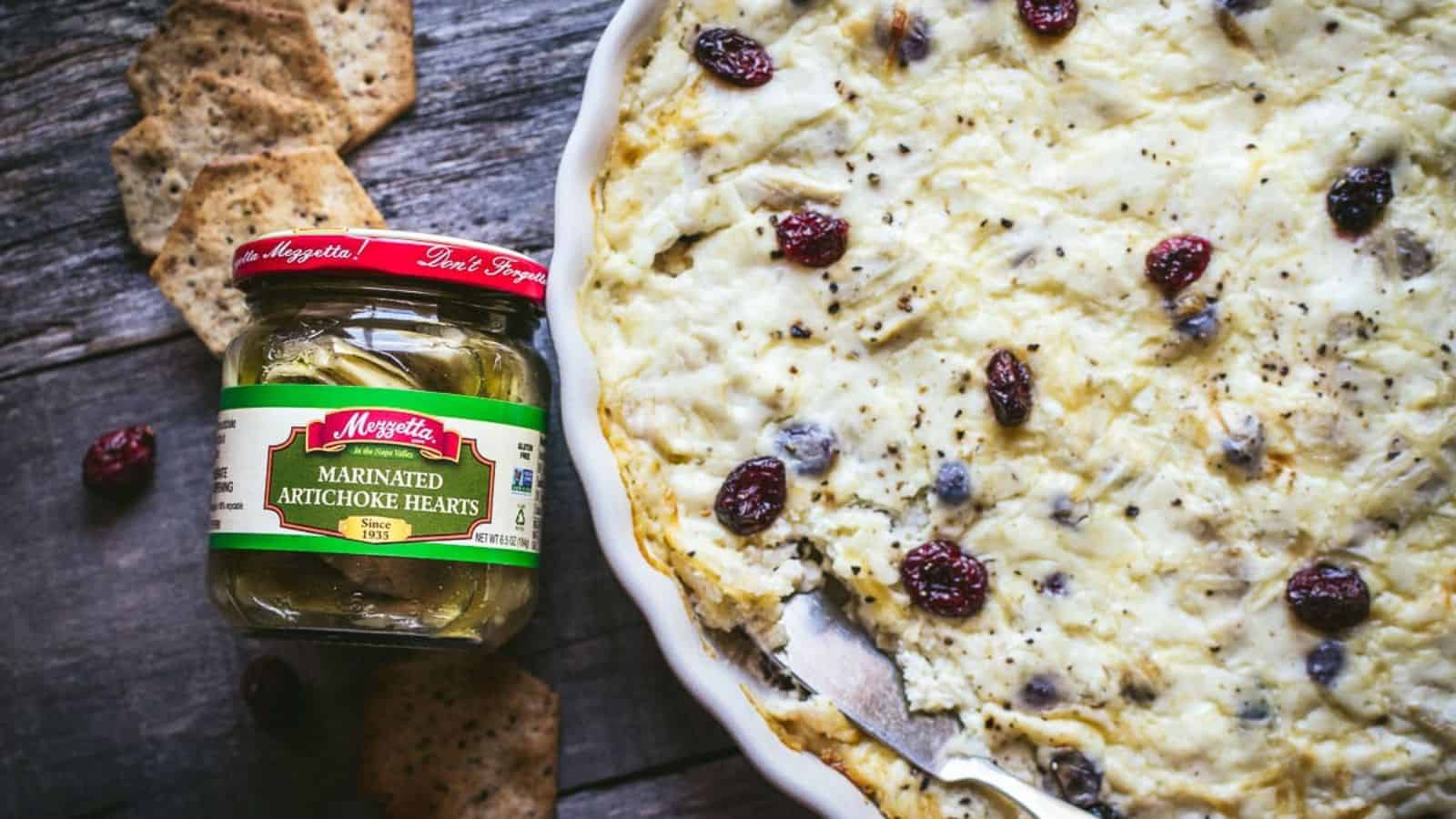 An image of Festive Cranberry Artichoke Dip next to a bottle of marinated artichoke hearts.