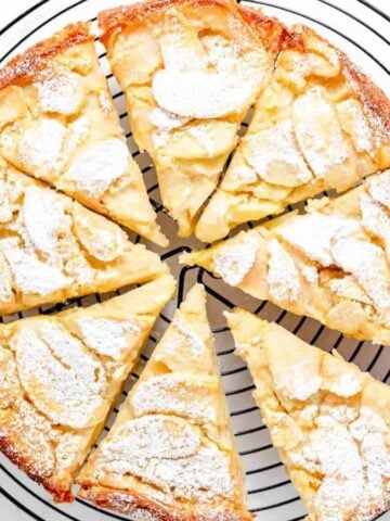 A whole, sliced French Apple Cake with green apples on the side.