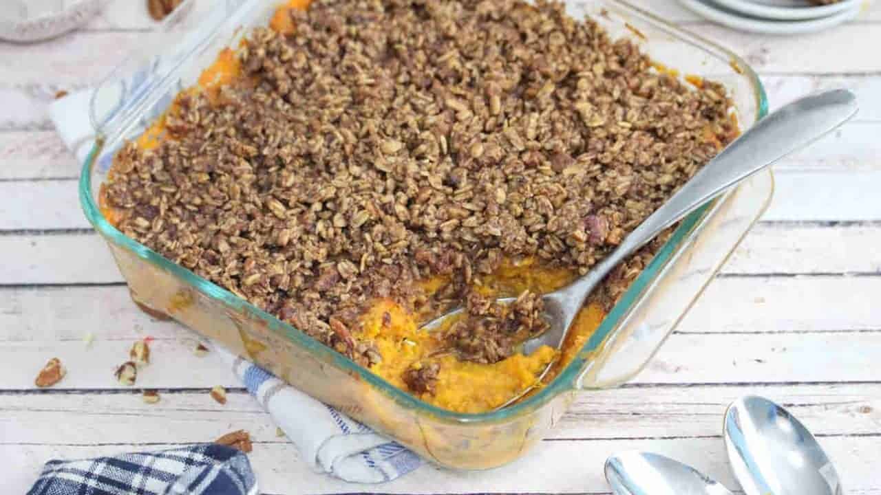 Sweet potato casserole with pecan topping in a glass baking dish with a spoon in the dish.