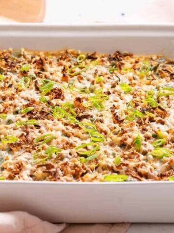 A Green Bean Casserole with Cream Cheese topped with a golden-brown crust and garnished with sliced green onions.