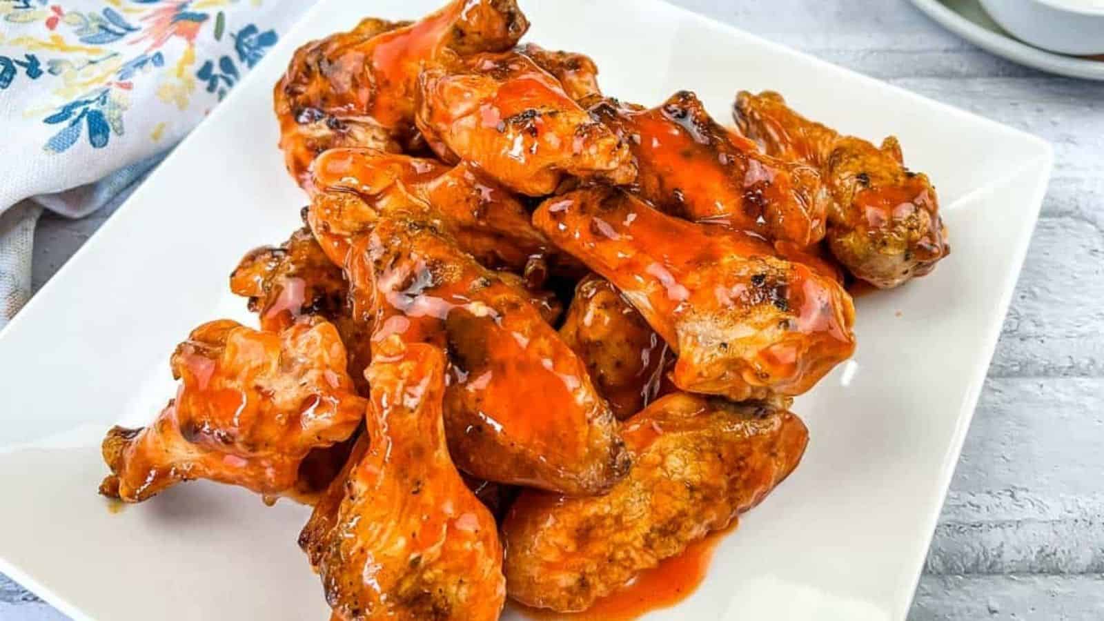 Chicken wings on a white plate with sauce and carrots.