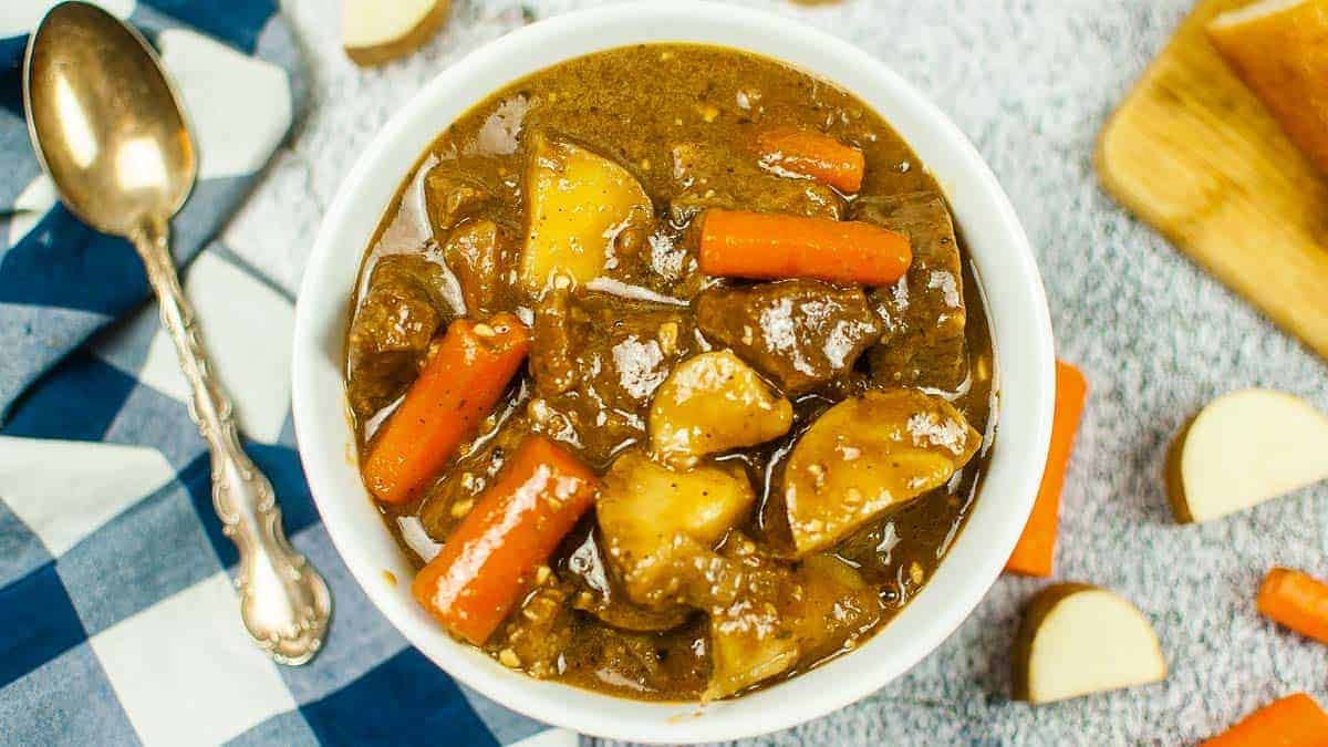 Top view of a bowl of Guinness beef stew with a black checked napkin and a spoon.