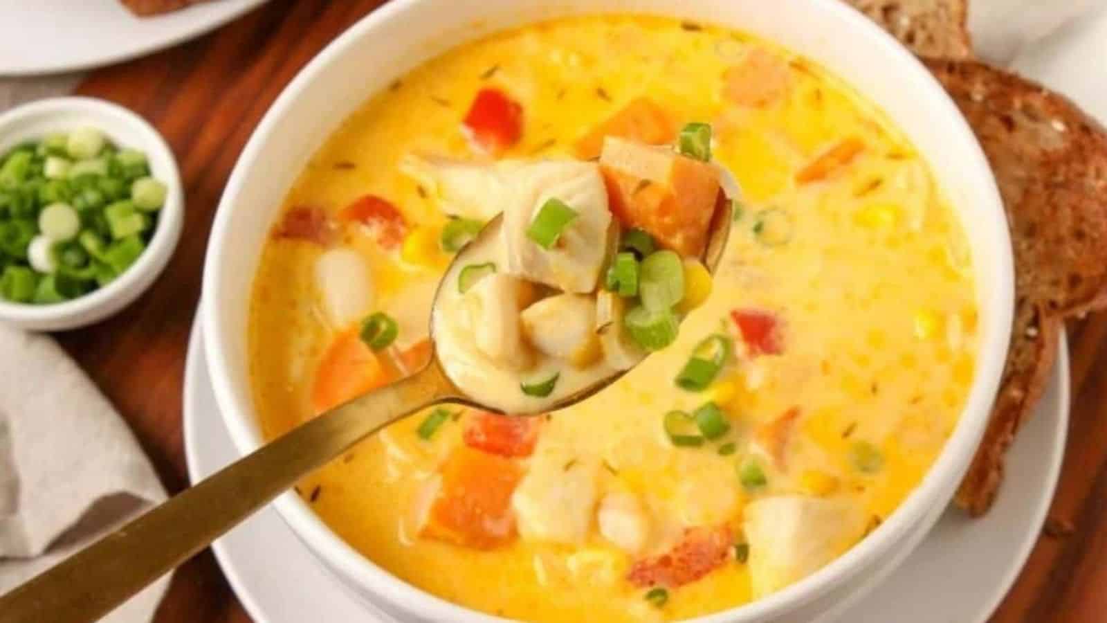 A bowl of seafood chowder with a spoon being held above it.