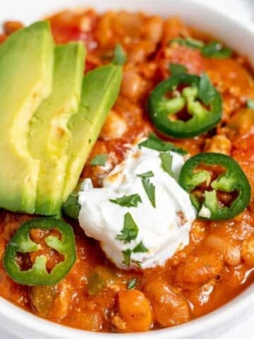 A bowl of chili topped with avocado and peppers.